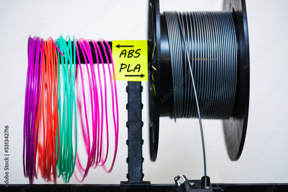 Loaded plastic filament on extruder with a sticky note that labels the variety of plastics used in 3d printing. - obrazy, fototapety, plakaty 