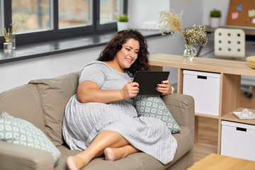 Wall Mural - technology, leisure and people concept - happy smiling woman with tablet pc computer on sofa at home