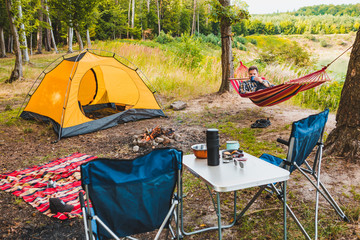 Wall Mural - man laying on hammock at lake beach near camp fire
