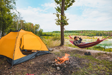 Wall Mural - man laying on hammock at lake beach near camp fire
