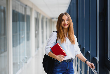 Wall Mural - Portrait of a pretty female student with books and a backpack in the university hallway