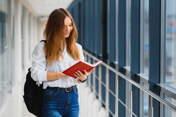 Wall Mural - Positivity beautiful girl smiling at camera, standing on corridor with notes as backpack, going to lesson. Happy brunette female student studying in luxury university.