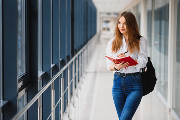 Wall Mural - Positivity beautiful girl smiling at camera, standing on corridor with notes as backpack, going to lesson. Happy brunette female student studying in luxury university.