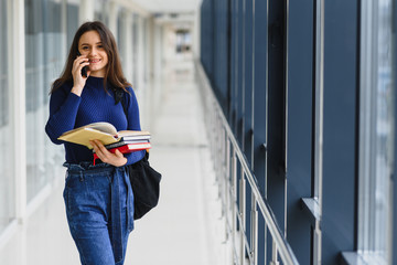 Wall Mural - Portrait of a pretty female student with books and a backpack in the university hallway