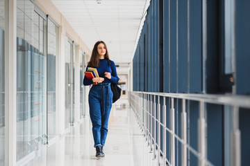 Wall Mural - Portrait of a pretty female student with books and a backpack in the university hallway