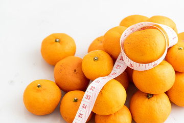 orange wrapped with measure tape  on white marble surface. Concept for fruit nutrition and diet food.