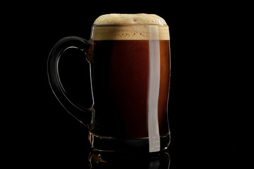 Beer mug with black stout on a black background. Isolated studio shot with reflection.