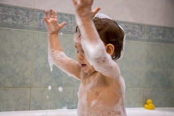 Wall Mural - Cute baby girl taking a bath. Funny toddler plays with soap foam in a bathtub. close up, soft focus, backgound green bathroom in blur