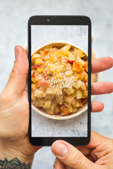 Wall Mural - Make photo of cooked, baked sweet apples cinnamon dessert with phone in woman hands. Smartphone food photography picture. Vegan, vegetarian healthy diet.