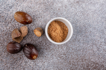 Nutmeg seed and ground nutmeg on concrete background. Freshly grated spice in white bowl. Close-up, copy space, top view.