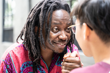 Black man with dreadlocks with a happy expression on his face holding the hand of a boy while they talk