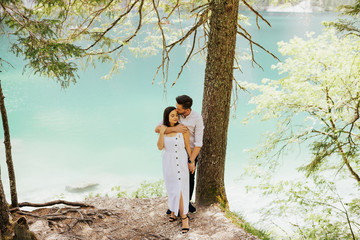 Wall Mural - The majestic azure color of Braies Lake in Italy. Couple standing at beach of mountain lake in Italy. Enjoying view. Summer passion crazy emotions photo on the seaside. 