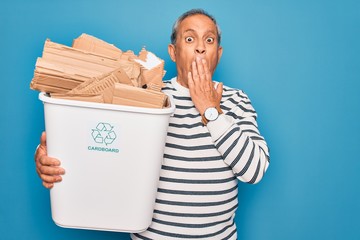 Poster - Senior man recycling holding trash can with cardboard to recycle over blue background cover mouth with hand shocked with shame for mistake, expression of fear, scared in silence, secret concept