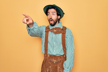 Wall Mural - Young handsome man wearing tratidional german octoberfest custome for Germany festival Pointing with finger surprised ahead, open mouth amazed expression, something on the front