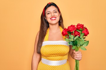 Young hispanic pin up woman wearing fashion sexy 50s style holding bouquet of red roses with a happy face standing and smiling with a confident smile showing teeth