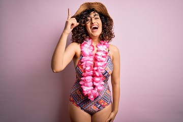 Sticker - Young beautiful arab woman on vacation wearing swimsuit and hawaiian lei flowers pointing finger up with successful idea. Exited and happy. Number one.