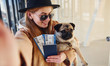 © standret - Young female passenger in warm clothes holding tickets and cute dog in hands in airport hall
