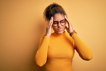 Poster - Young beautiful african american girl wearing sweater and glasses over yellow background with hand on headache because stress. Suffering migraine.