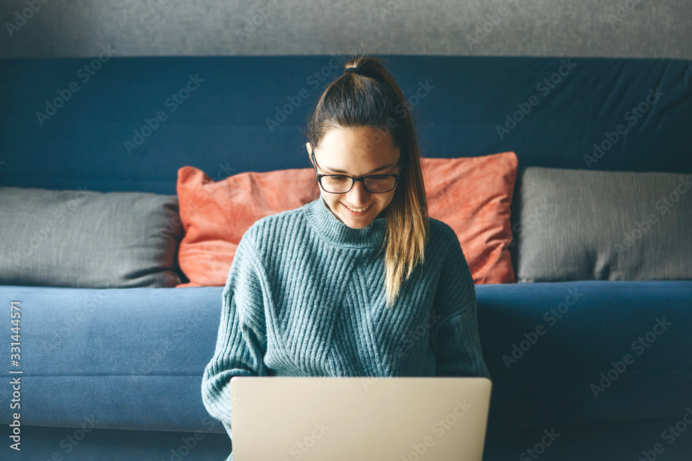 Girl working on laptop from home or student studying from home or freelancer. Or she is watching a video or using the Internet - obrazy, fototapety, plakaty 