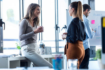 Two business young woman drinking coffee while taking a break on coworking space.