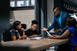 © JonoErasmus - African businessman talking with a diverse group of female colleagues while having a meeting together around a table in an office boardroom