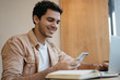 © ARUTA Images - Indian freelancer holding smartphone, communication, working from home. Handsome asian man using laptop computer, internet, planning project, sitting in modern office