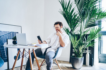 Cheerful freelancer using mobile phone in creative hall