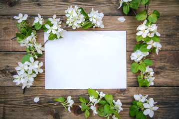 Poster - A branch of a blooming apple tree with white flowers and a sheet of paper on a wooden background, with a copy space