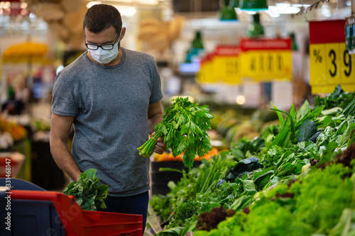 Alarmed male wears medical mask against coronavirus while grocery shopping in supermarket or store- health, safety and pandemic concept - young man stockpiling food in fear of covid-19