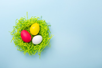 Cute Easter composition. Paper nest with multicolored easter eggs on blue background. Top view. Copy space