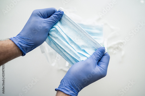 Doctor, nurse or scientist hand in blue nitrile gloves holding a medical face mask for protection against infection. Covid-19 coronavirus with stop sign Earth in medical mask quarantine