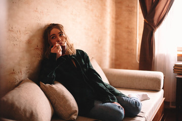 Wall Mural - Young thoughtful woman drinking tea while sitting on sofa in living room at home