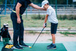 © Microgen - Golf Lessons. Golf instructor giving game lesson to a young boy.