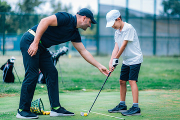 personal golf lesson. golf instructor with young boy on a golf driving range.