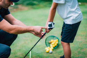 golf instructor adjusting young boy’s grip