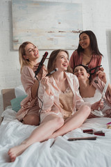Wall Mural - Selective focus of multiethnic women putting makeup and doing hairstyles at bachelorette party on bed