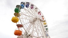 Low Angle Shot Of Slowly Moving Ferris Wheel With Colorful Pods. Empty Amusement Ride, At Fairground, No People Seen In Open Gondolas