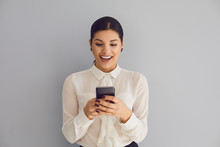 Using The Phone On Social Networks. Hispanic Young Happy Woman Typing Sms In Mobile Smiling While Standing On Gray Background.