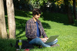 © ianachyrva - Young bearded brunet student with mustache sitting with a laptop in a park on grass