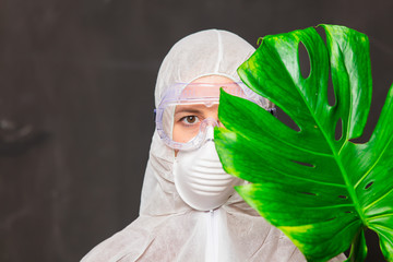 female doctor in protection suit and glasses with mask holds palm leaf