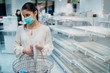 © eldarnurkovic - Young person with protective face mask buying groceries/supplies in the supermarket.Food supplies shortage.Empty shelves in the store due to novel coronavirus covid-19 (2019-nCoV) outbreak panic