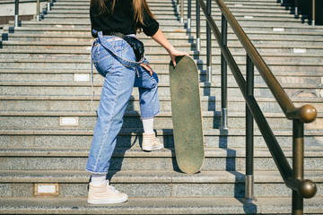 Urban woman with skate. Hipster girl with skateboard in city. Extreme sport and emotions concept. Alternative lifestyle. Stylish hipster girl holding skateboard and posing. Street style outfit