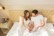 © rilueda - Attractive young couple sitting on a hotel bed and reading news from tablet pc