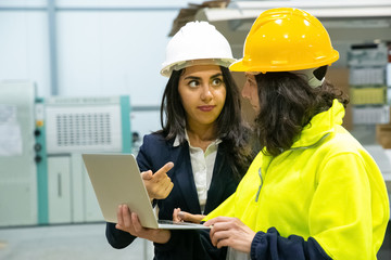 Wall Mural - Confident women with laptop at manufacturing plant. Two female employees talking while standing at factory with laptop. Print manufacturing concept