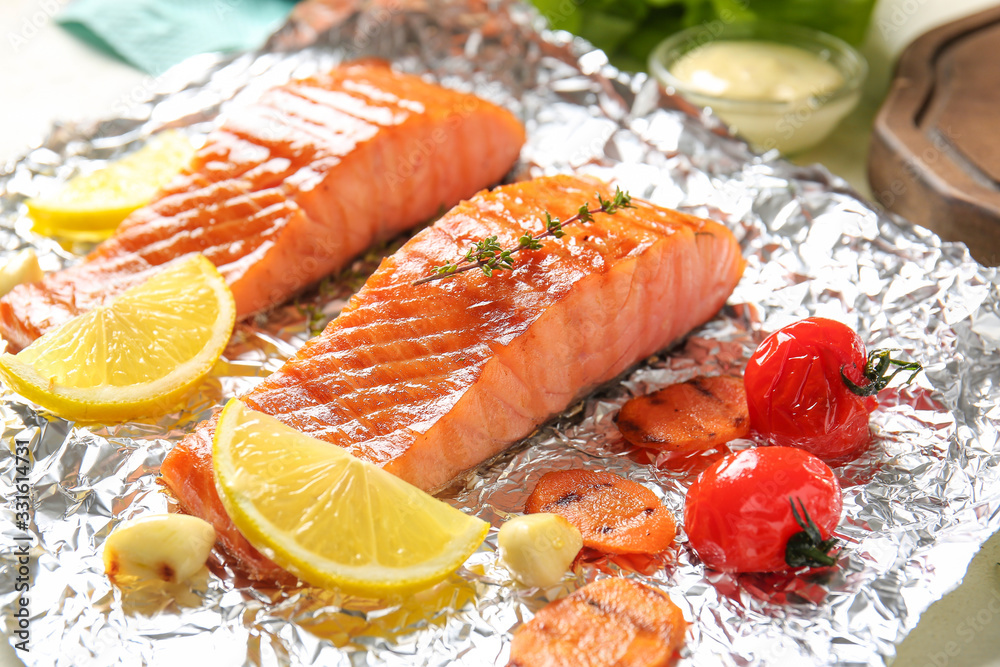 Foil with cooked salmon fillet and vegetables on table, closeup