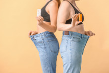 Women In Loose Jeans And With Weight Loss Pills On Color Background