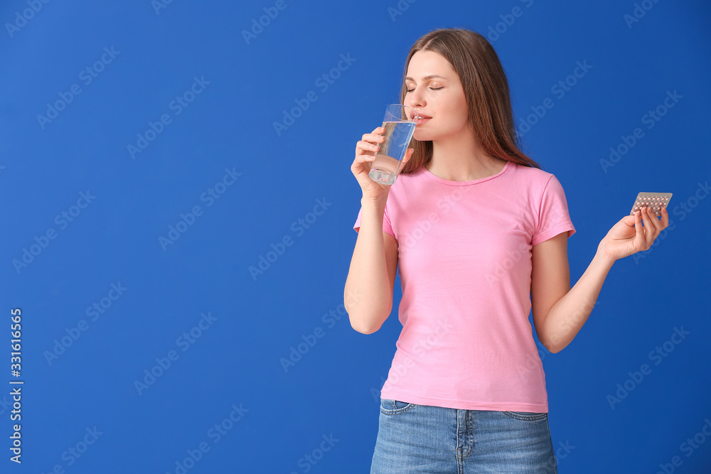 Young woman taking birth control pills on color background