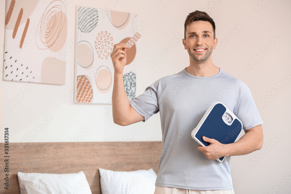 Young man with weight loss pills and scales at home