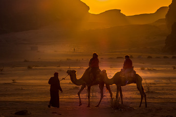 A bedouin riding 2 tourists on a camel at sunrise in the desert..Jordan, Wadi Ram