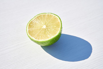 Wall Mural - Ripe lime half on white wooden background, close-up shot in harsh sunlight with long colored shadows.